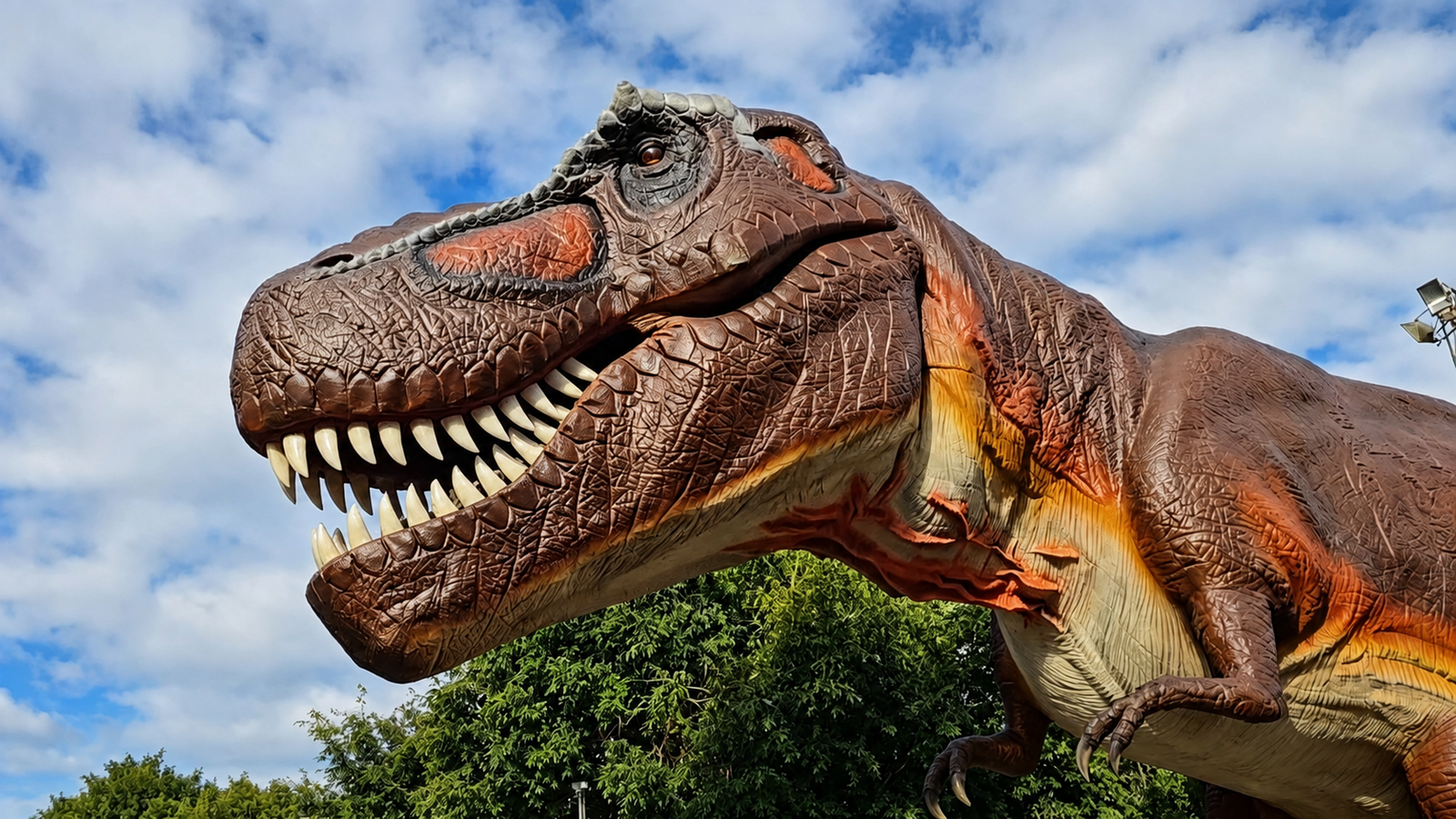 Una réplica a gran escala de un dinosaurio animatrónico sobre el césped rodeado de árboles y carteles informativos.