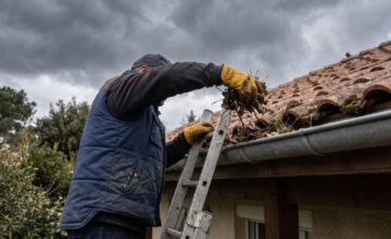 Persona realizando mantenimiento y limpieza en las canaletas del techo de una casa.